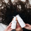 Woman with healthy defined curly hair holding cadó Leave-in Conditioner and Curl Defining Foam for professional curly hair care routine.