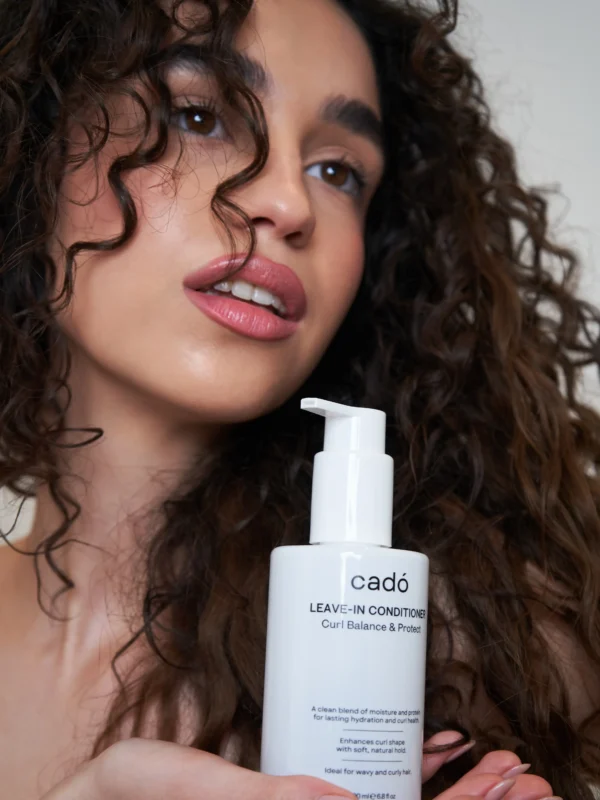 Model holding cadó Leave-in Conditioner showcasing hydrated and frizz-free natural curls.