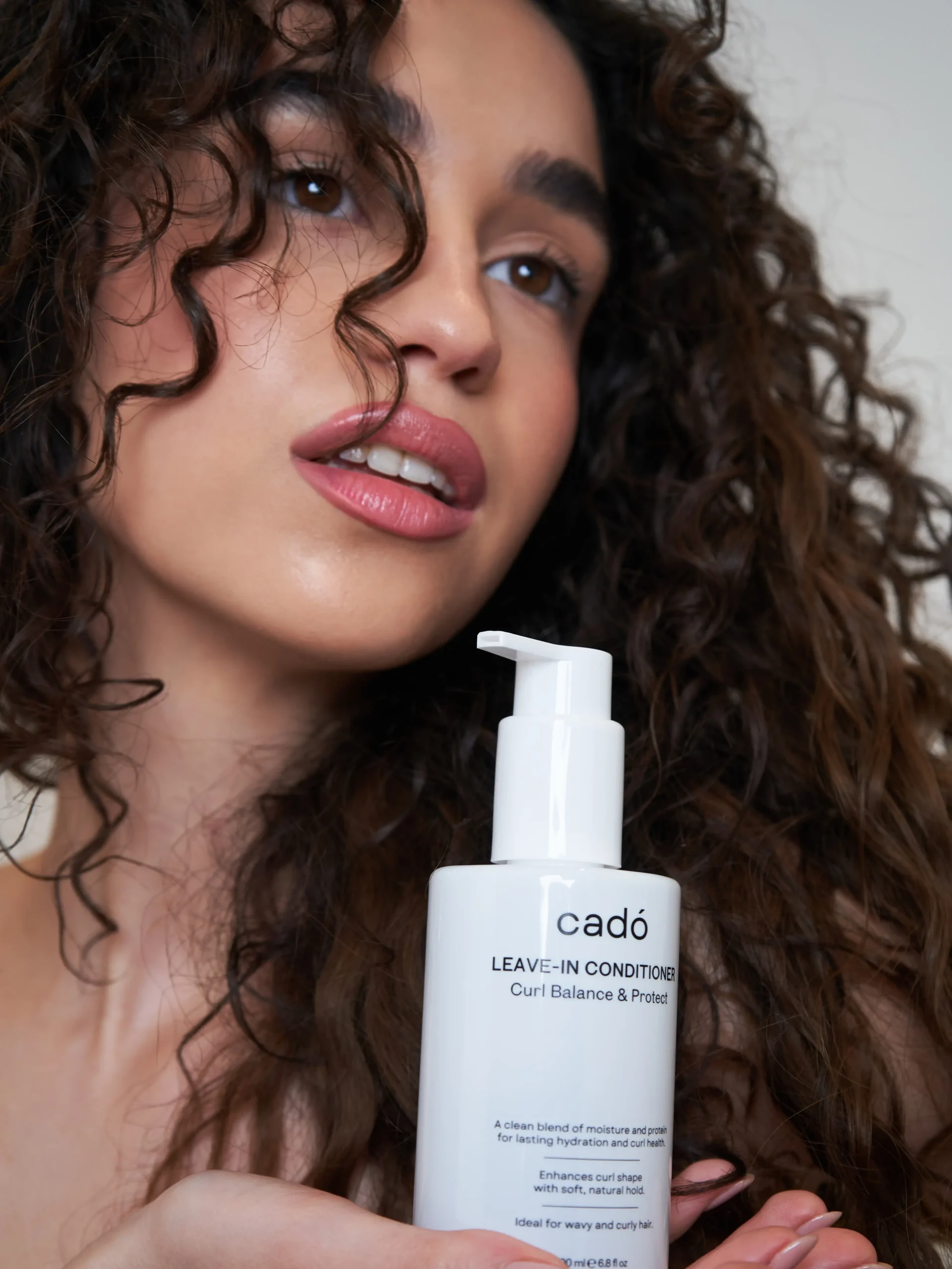 Model holding cadó Leave-in Conditioner showcasing hydrated and frizz-free natural curls.