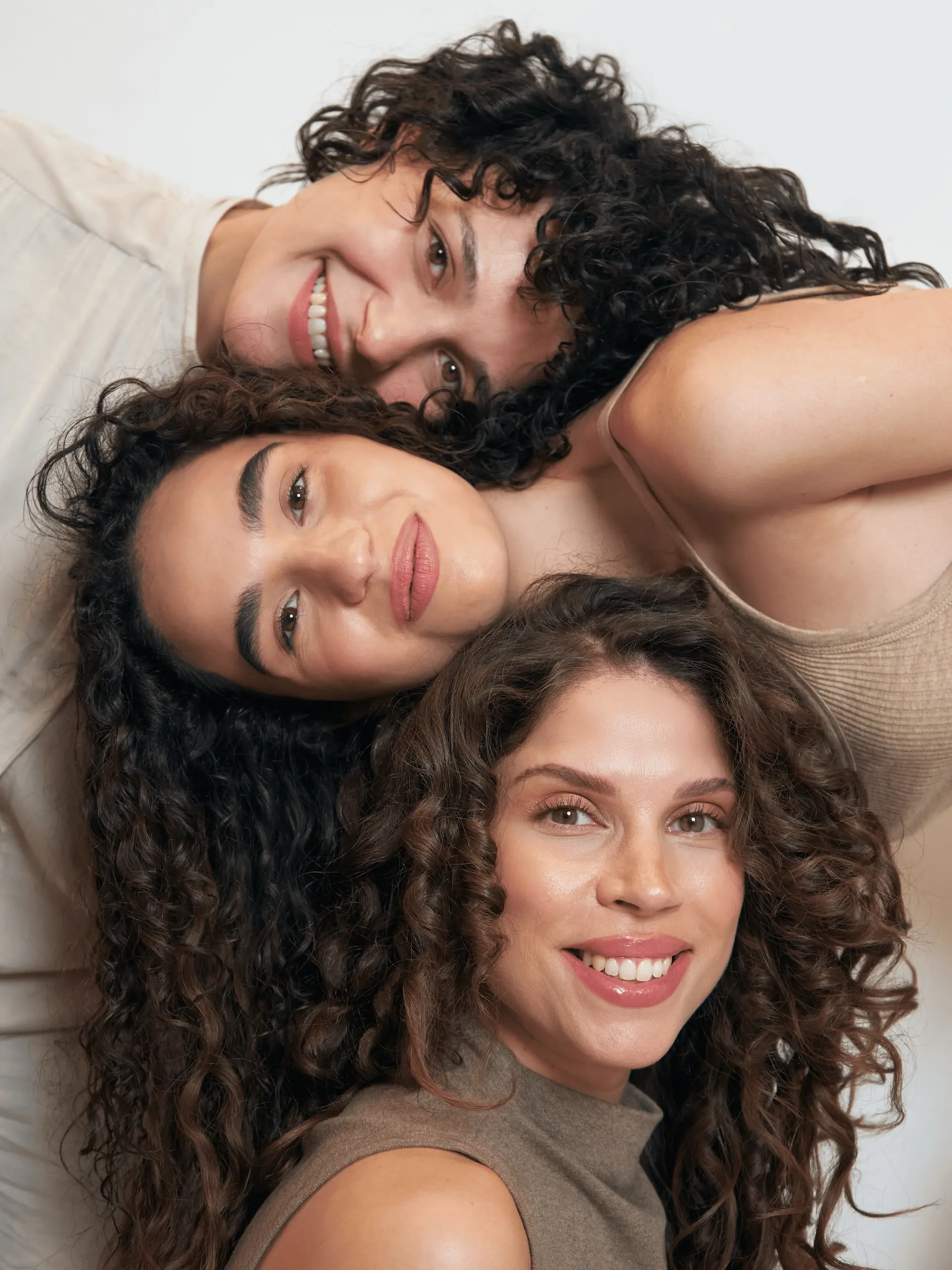 A group of diverse women smiling and showing their healthy, defined curls after their cadó professional hair care ritual.